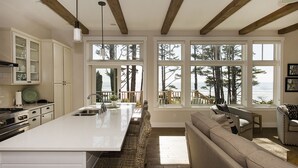 A kitchen with a large island, wooden beams, and a view of the ocean through large windows.