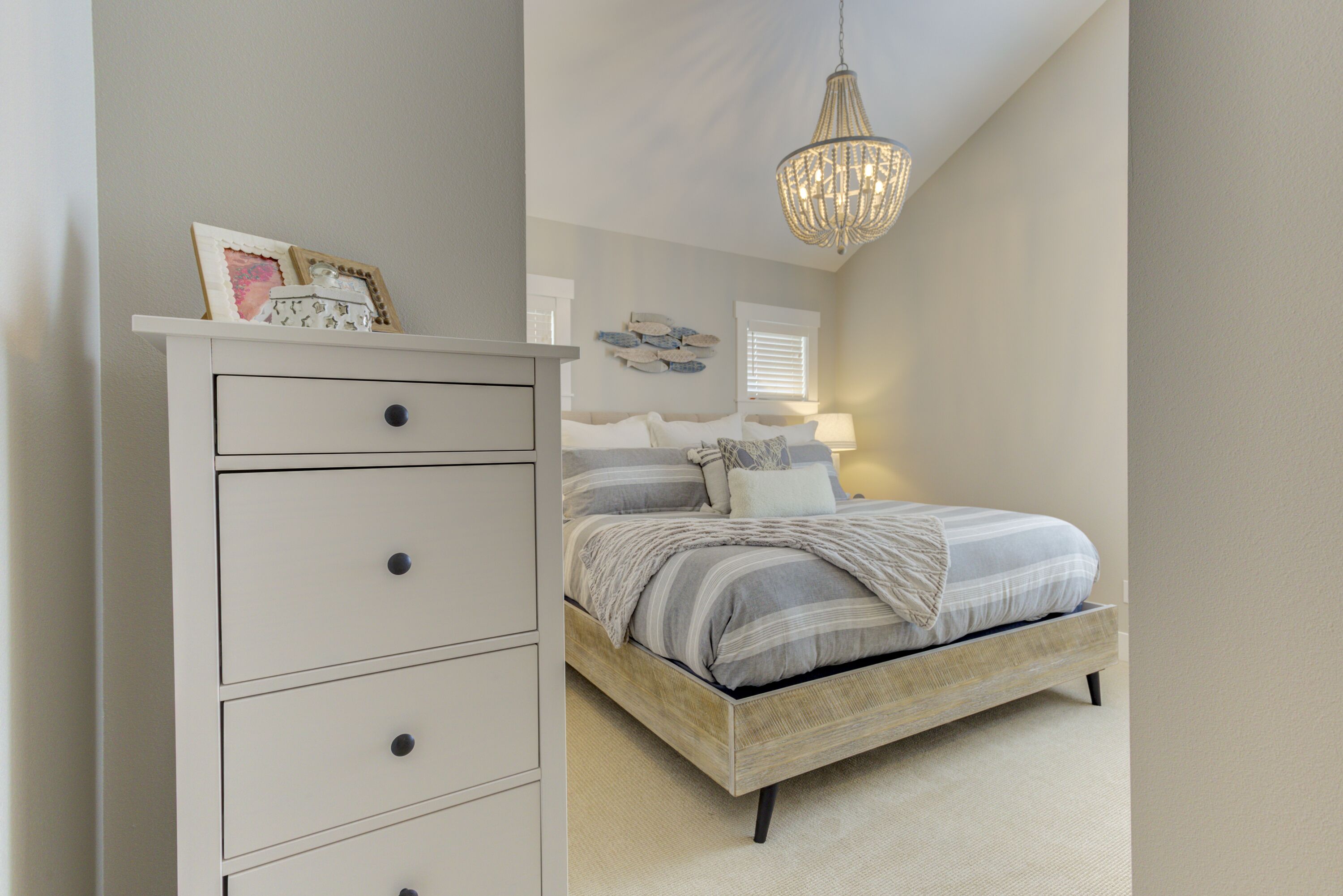A bedroom with a bed, dresser, and chandelier.