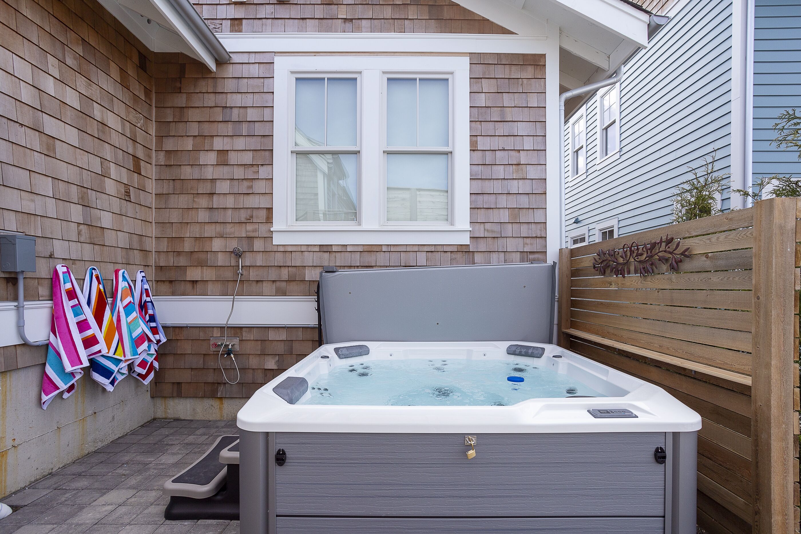 Un jacuzzi en un patio trasero con valla de madera, una ventana y toallas de colores colgadas en la pared.