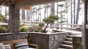 A cozy outdoor seating area with a stone bench, a wooden rocking chair, and a stone fireplace. - *New* Seabrook's Togadera: Luxury ocean front home! (Pacific Beach)