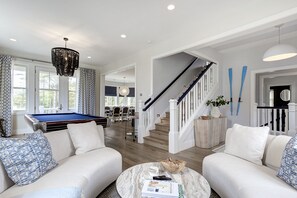 A spacious living room with a pool table, a staircase, and a dining area.