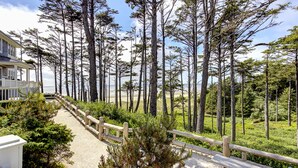 A pathway leading through a forested area with a wooden fence, surrounded by tall trees and a building with a balcony. - *New* Seabrook's Togadera: Luxury ocean front home! (Pacific Beach)