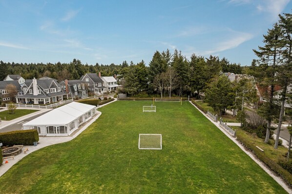 Un grand terrain herbeux bien entretenu, avec deux buts de football, entouré de maisons et d’arbres.