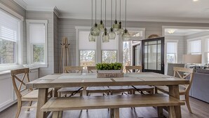 Un comedor con mesa y bancos de madera, lámparas colgantes y vistas al exterior a través de amplios ventanales.