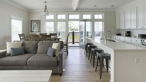 Amplia sala de estar con un sofá gris, una mesa de comedor y una cocina con armarios blancos y un ventanal grande.