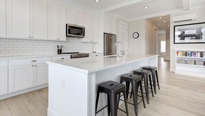 Una cocina moderna con armarios blancos, una isla central con taburetes de bar, electrodomésticos de acero inoxidable e iluminación empotrada.