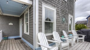 Una terraza de madera con sillas Adirondack blancas y una zona cubierta con un reloj.