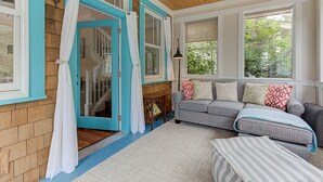 Un accogliente soggiorno con soffitto in legno, un divano grigio con cuscini decorati, un tappeto bianco e una porta con cornice blu.