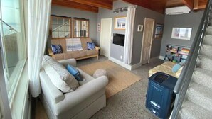 Ein gemütliches Wohnzimmer mit einer Couch, einem kleinen Tisch und einem Fernseher. Eine Treppe führt zu einer weiteren Ebene.