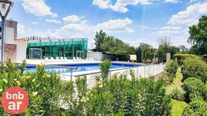 A swimming pool with lounge chairs, a modern building with glass windows, and lush greenery. - Beautiful condo with Swimming Pool  and 24/7 security (Córdoba)