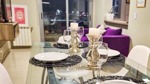 A dining table set with plates, glasses, and candles, surrounded by purple cushions and a glass partition. - Beautiful condo with Swimming Pool  and 24/7 security (Córdoba)