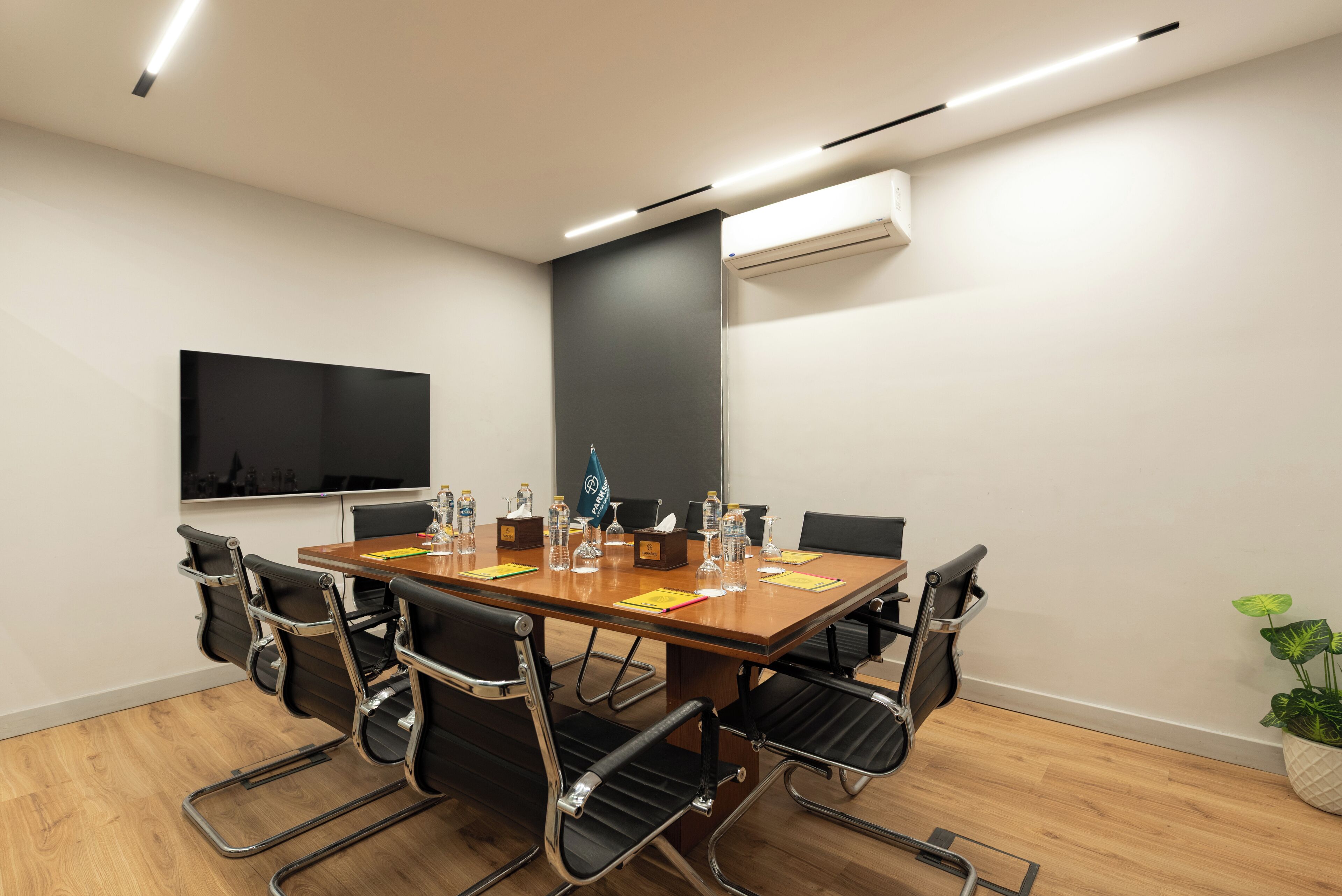 A conference room with a long table, black chairs, a flat-screen TV, and an air conditioning unit on the wall.