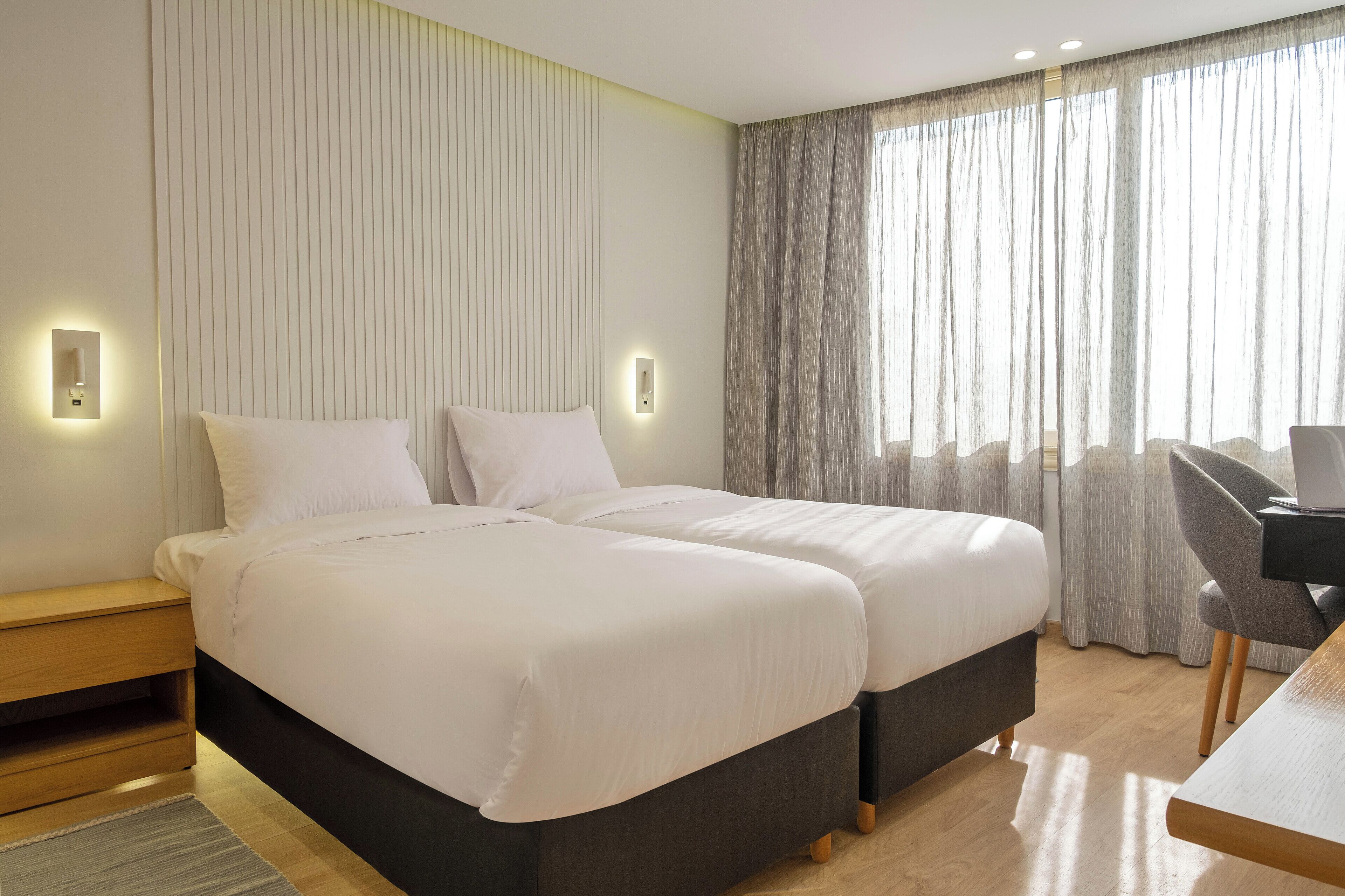 Et hotelværelse med to senge, et skrivebord og en stol.