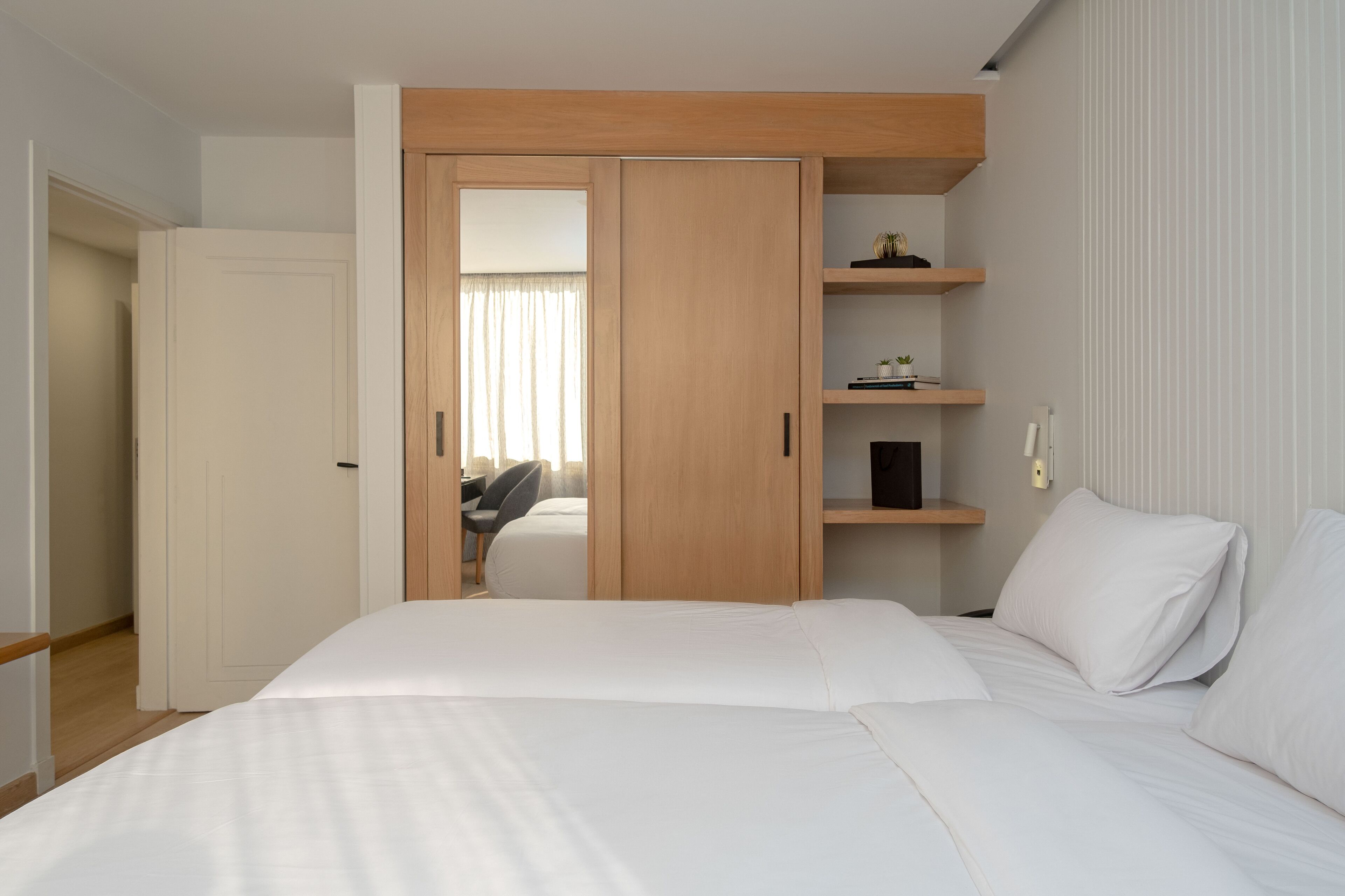 A bedroom with a large bed, a wardrobe with a mirror, and a desk with a chair.