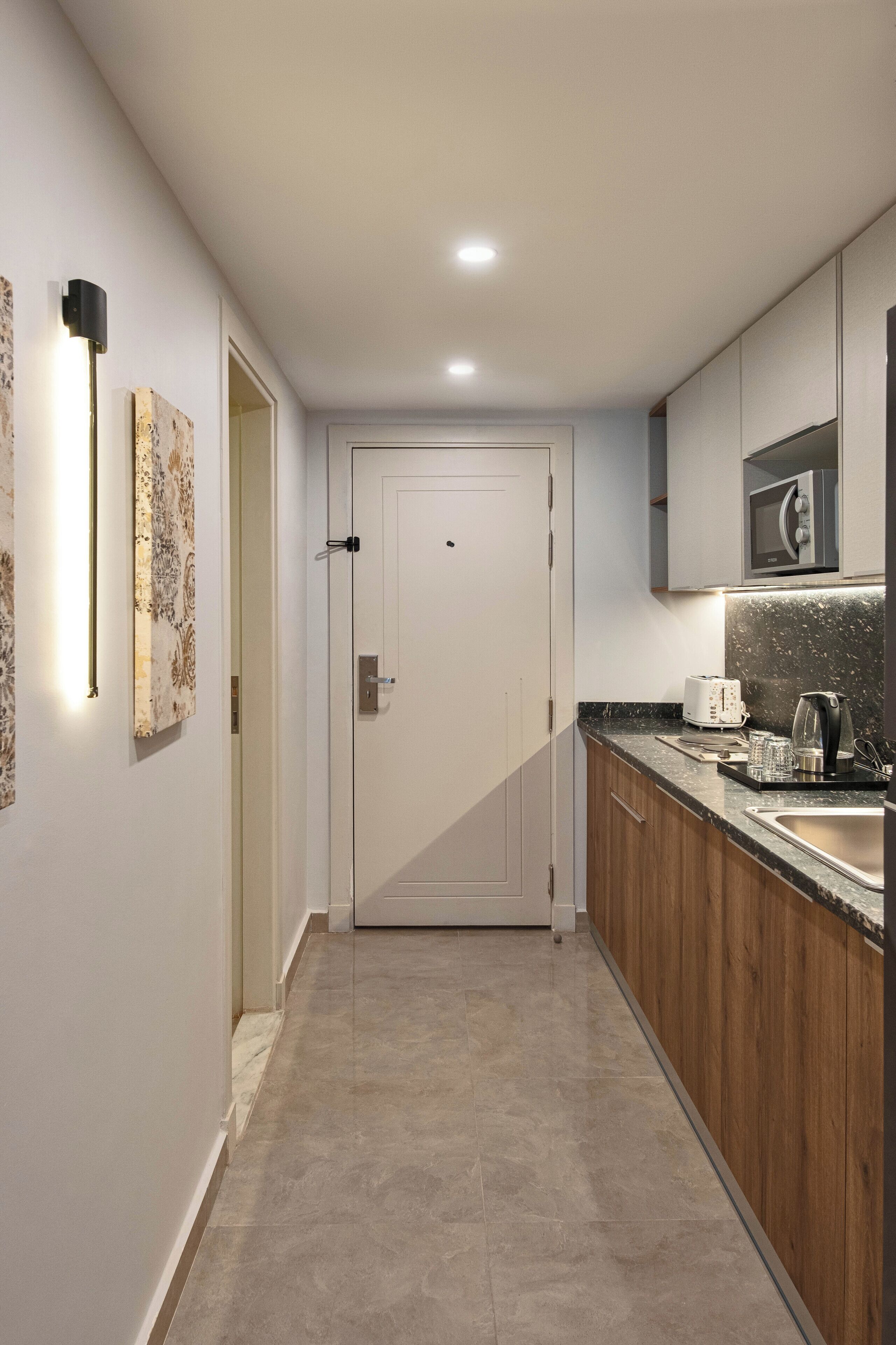 A modern kitchen with a white door, wooden cabinets, a granite countertop, and a microwave.