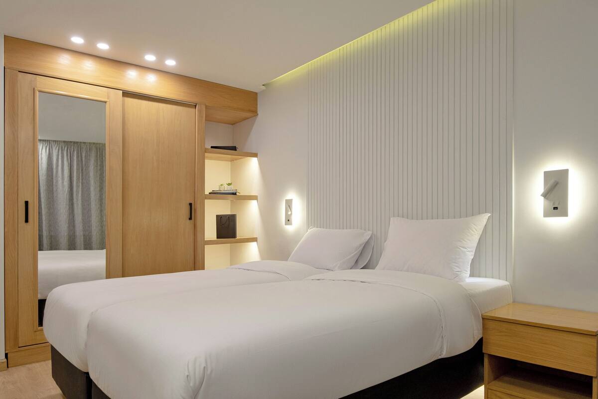 A modern bedroom with a large bed, built-in wardrobe, bedside tables, and wall-mounted lighting.