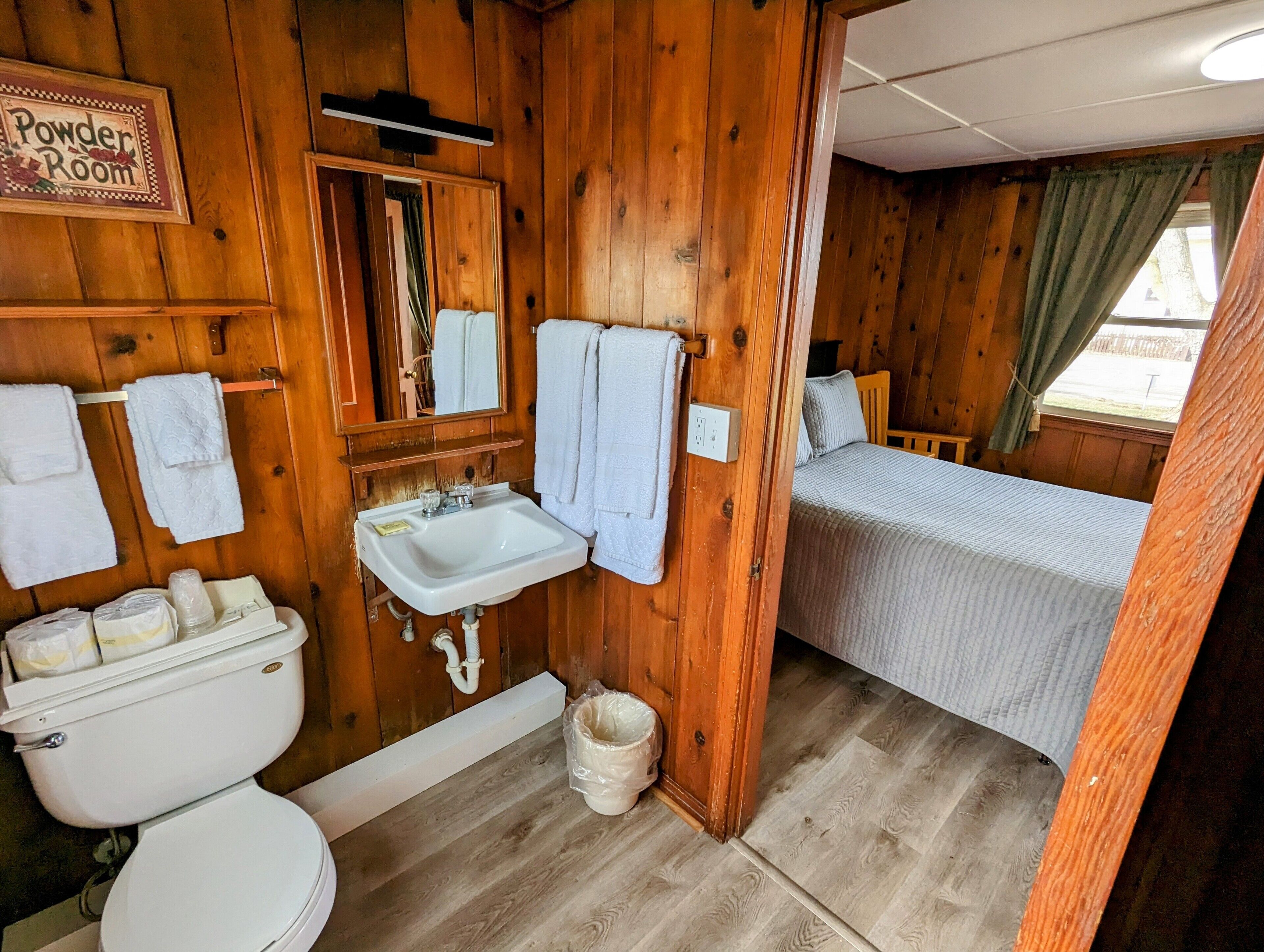 A wooden cabin bathroom with a toilet, sink, and a bed.