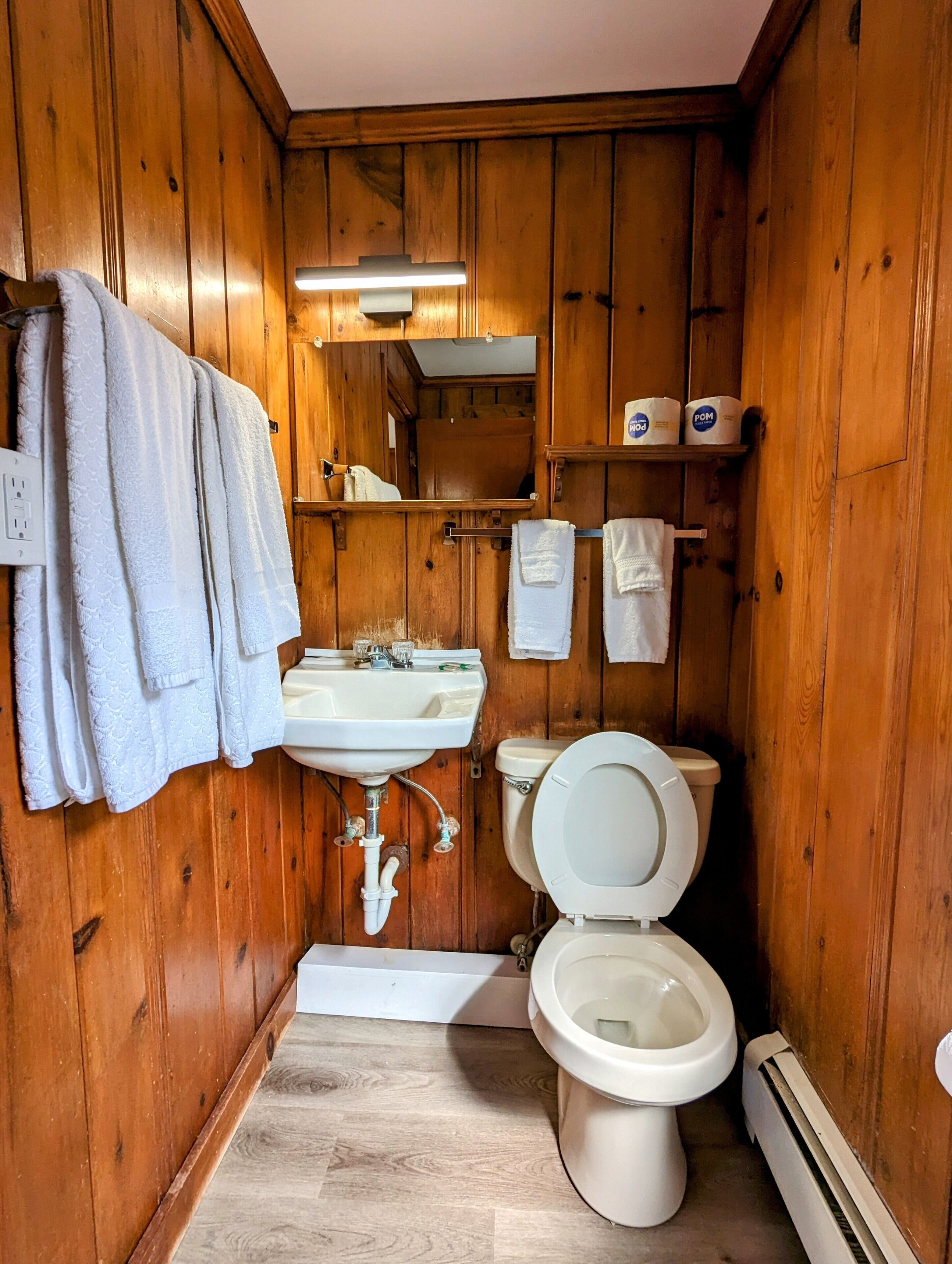 A wooden-paneled bathroom with a white sink, toilet, and towel rack.