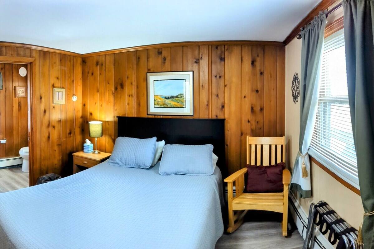 A hotel room with two beds, a television, a desk with a computer, and a window with curtains.