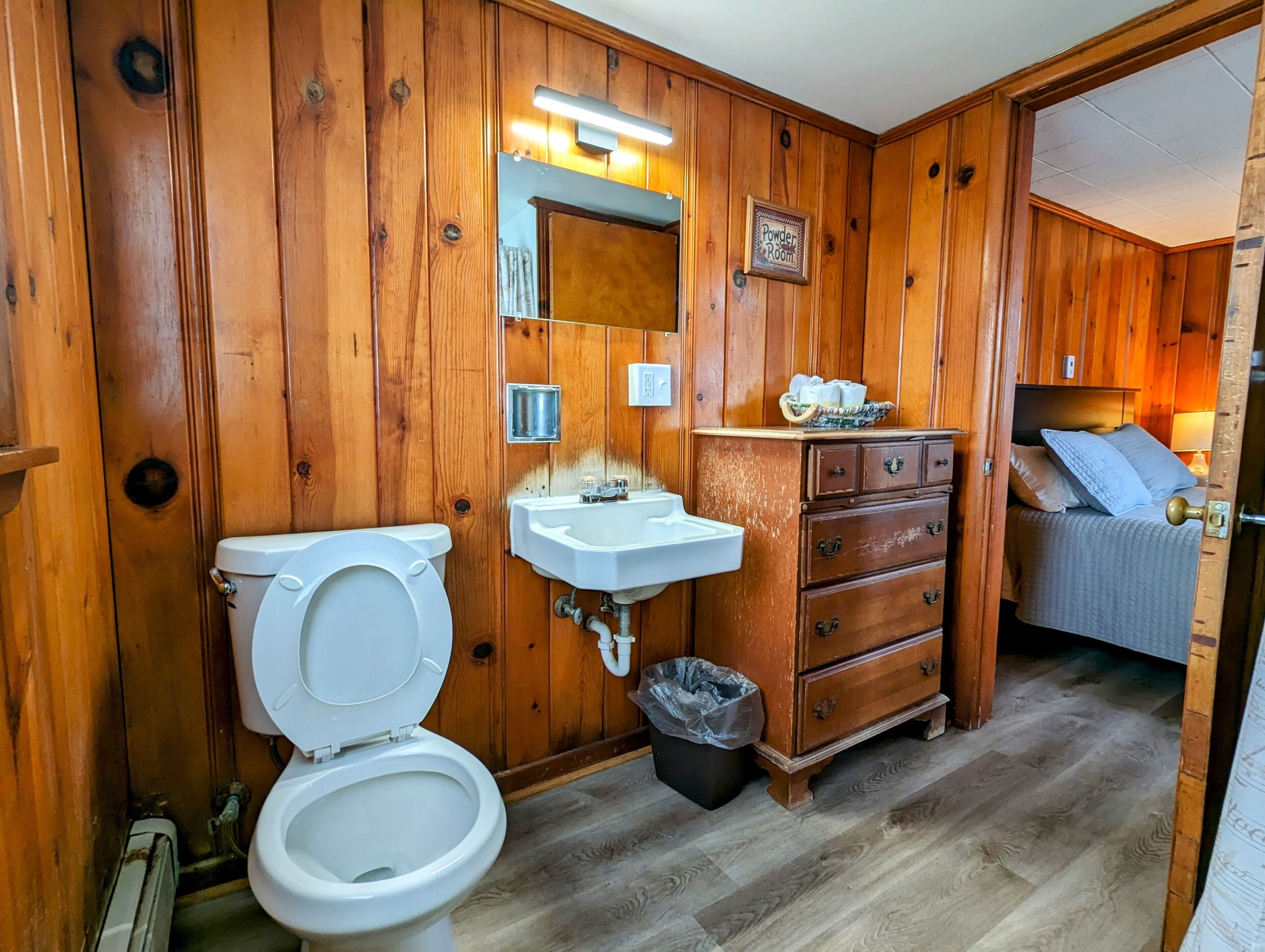 A wooden-paneled bathroom with a toilet, sink, and a bed with a headboard.