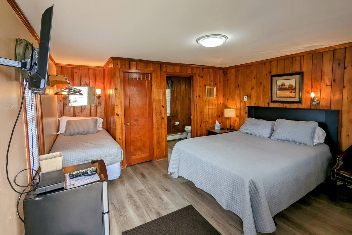 A room with two beds, wooden walls, a ceiling light, and a television.