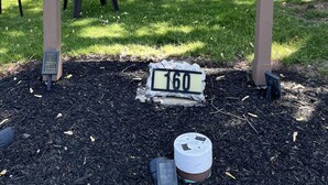 A sign for Riverside Motel with a fish logo, a number '160' plaque, and a house in the background. - Riverside Motel (Lewiston)