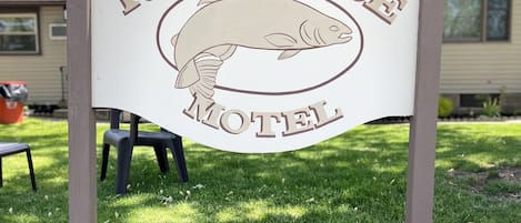 A sign for Riverside Motel with a fish logo, a number '160' plaque, and a house in the background.