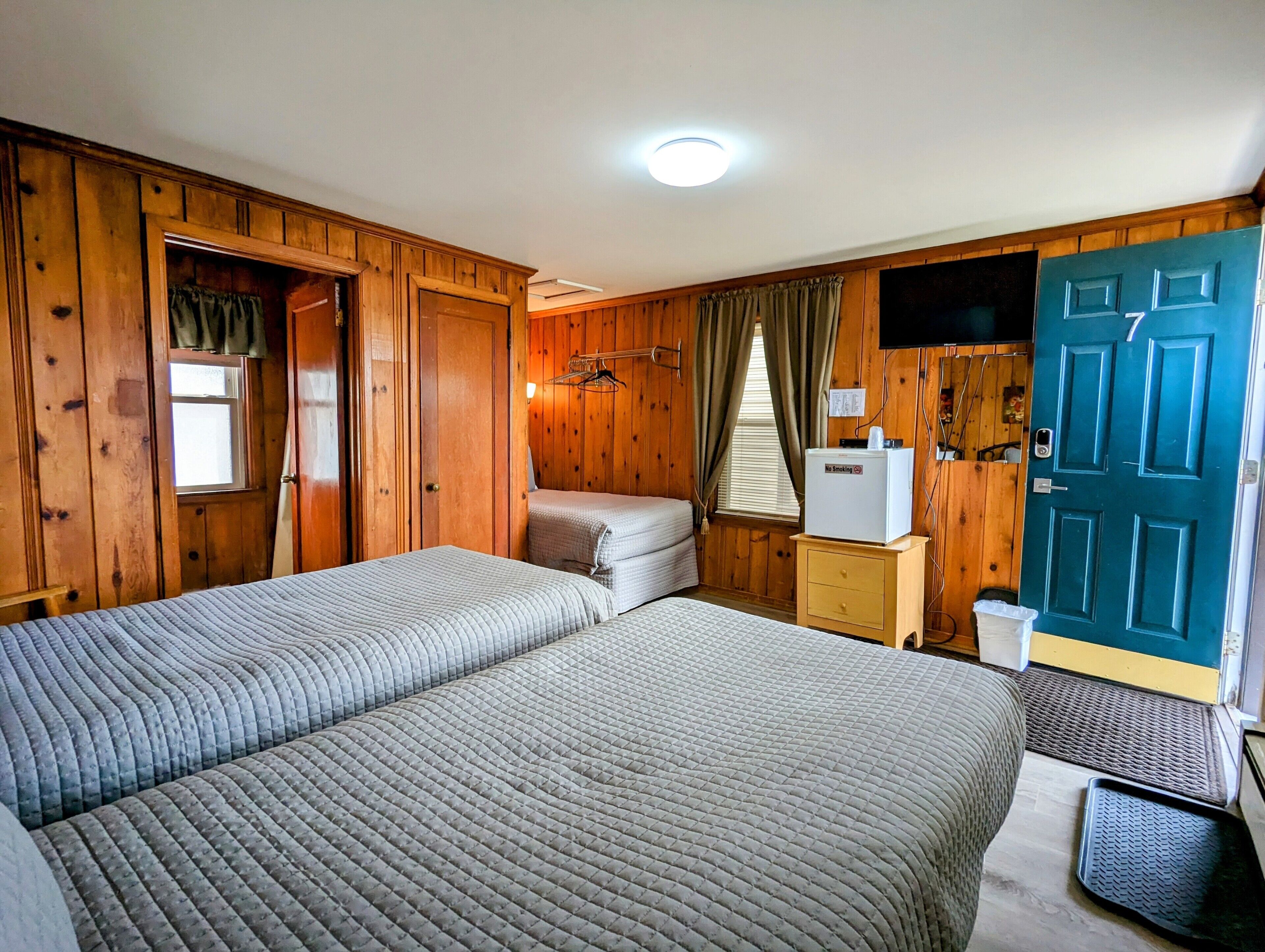 A room with two beds, wooden walls, a TV, a door, and a small cabinet.