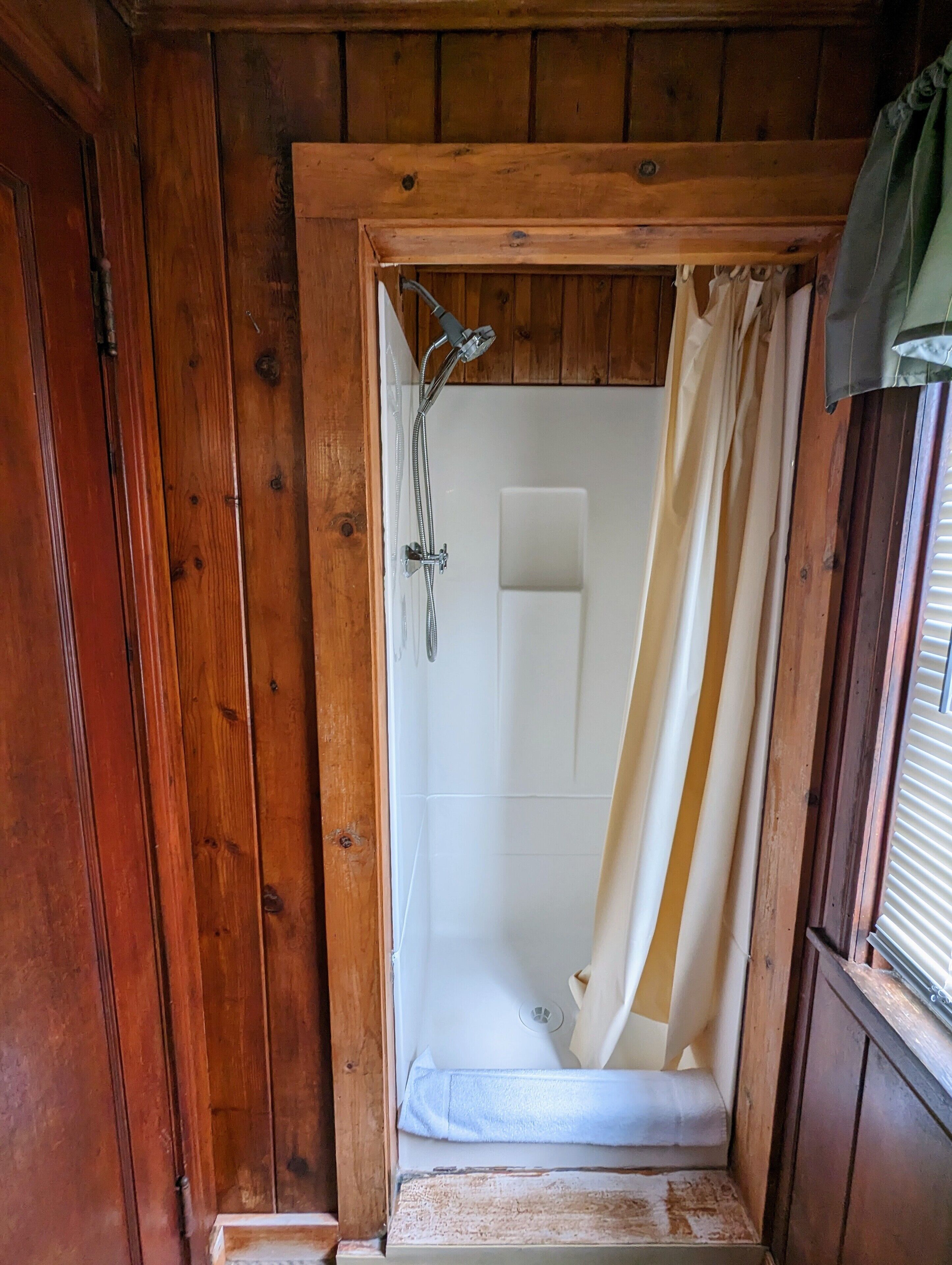 A wooden-framed shower with a white tiled wall and a shower curtain.