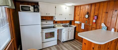 Una cocina compacta con electrodomésticos blancos, paneles de madera y un pequeño comedor.