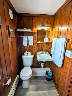 A compact wooden bathroom with a toilet, sink, and mirror.