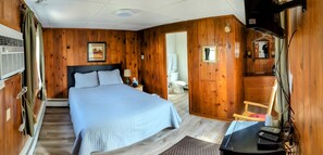 A wooden-paneled room with a bed, a nightstand, a mirror, and a hanging coat rack. - Riverside Motel (Lewiston)