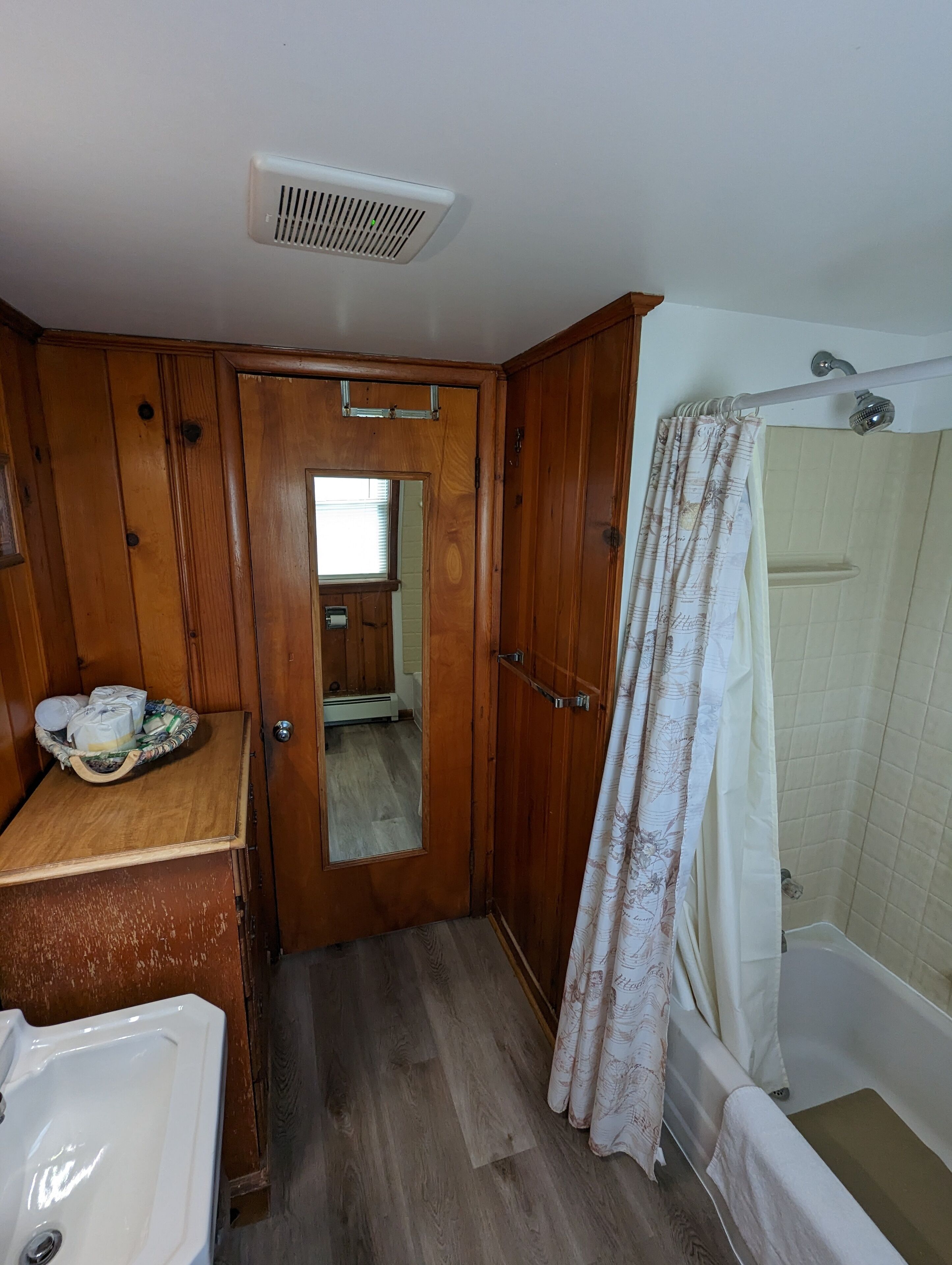 Ein Badezimmer mit einem Holzbadschränkchen, einem Waschbecken, einer Duschkabine und einem Spiegel.