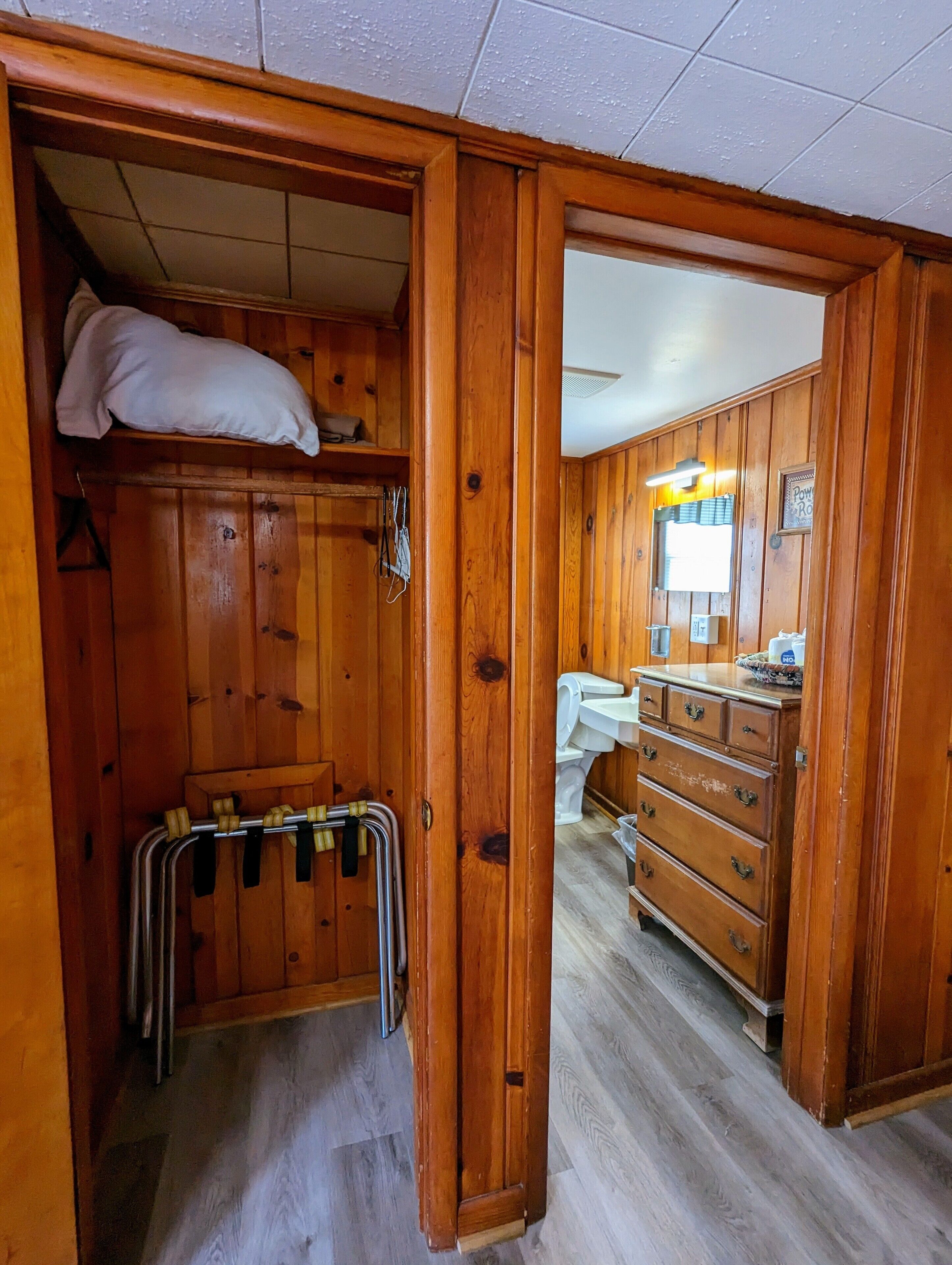 A wooden-paneled room with a bed, a dresser, and a bathroom with a sink and mirror.