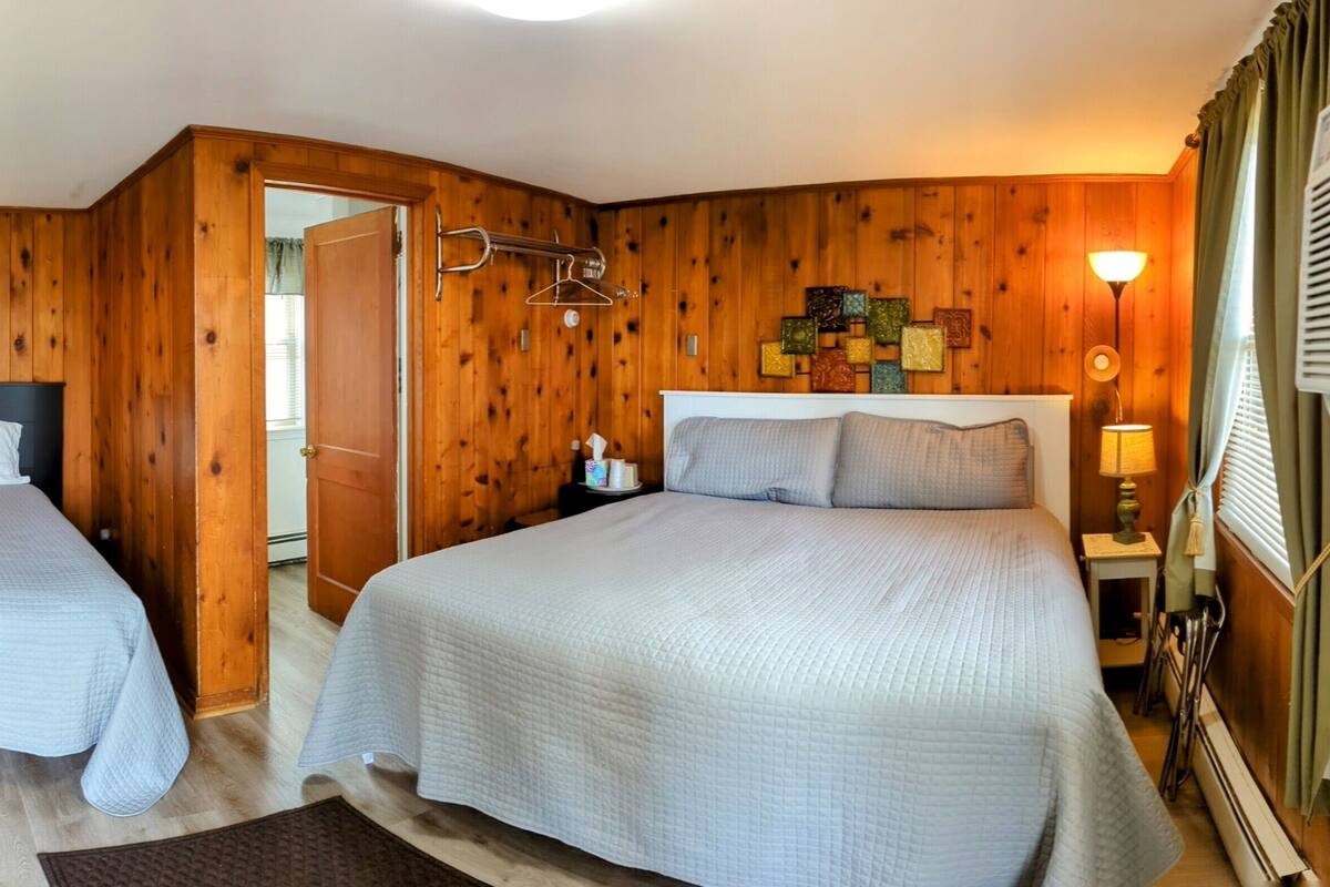 A room with two beds, wooden walls, a TV, and a small desk.