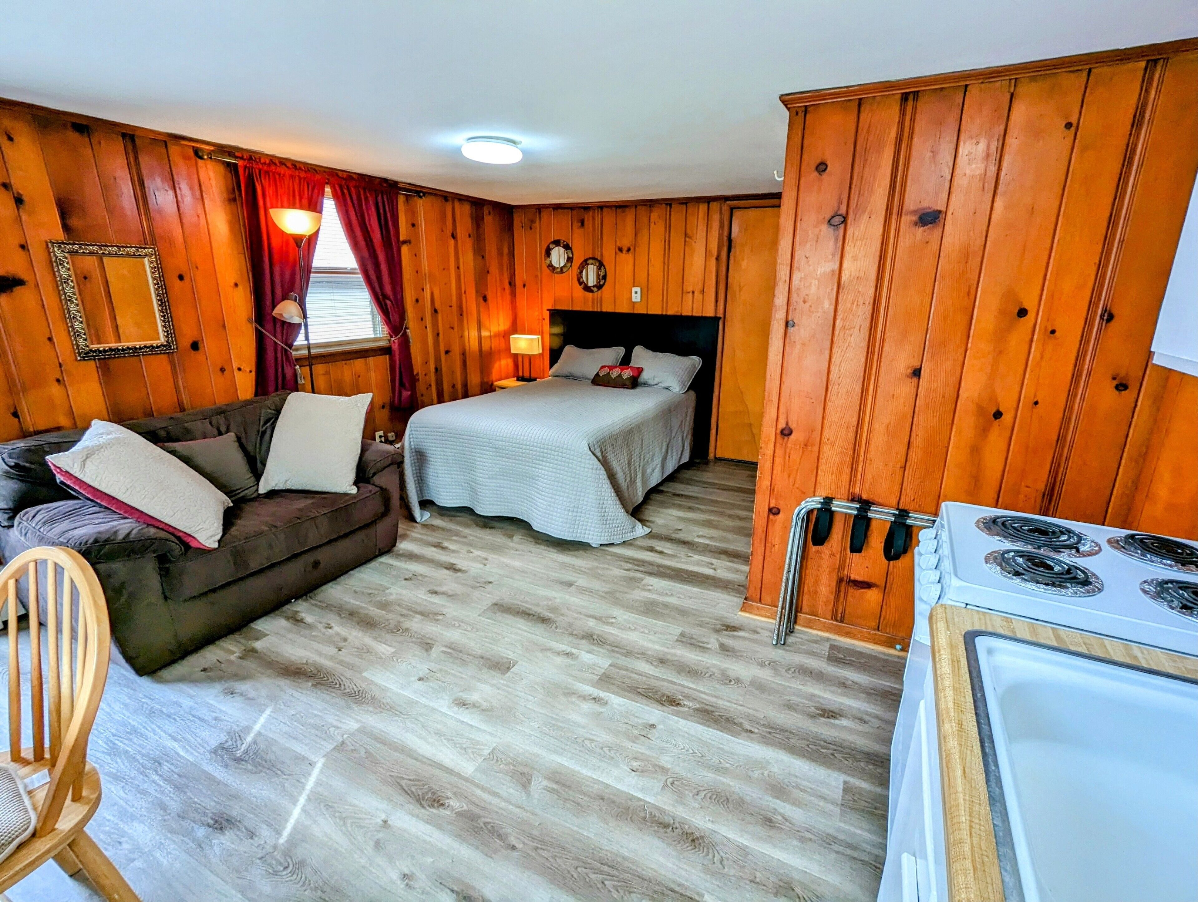 A cozy cabin-style room with a bed, a couch, a chair, and a kitchenette.