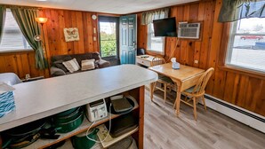 A cozy cabin with a wooden interior, a dining area with a table and chairs, a sofa with cushions, a TV mounted on the wall, and a window with curtains. - Riverside Motel (Lewiston)