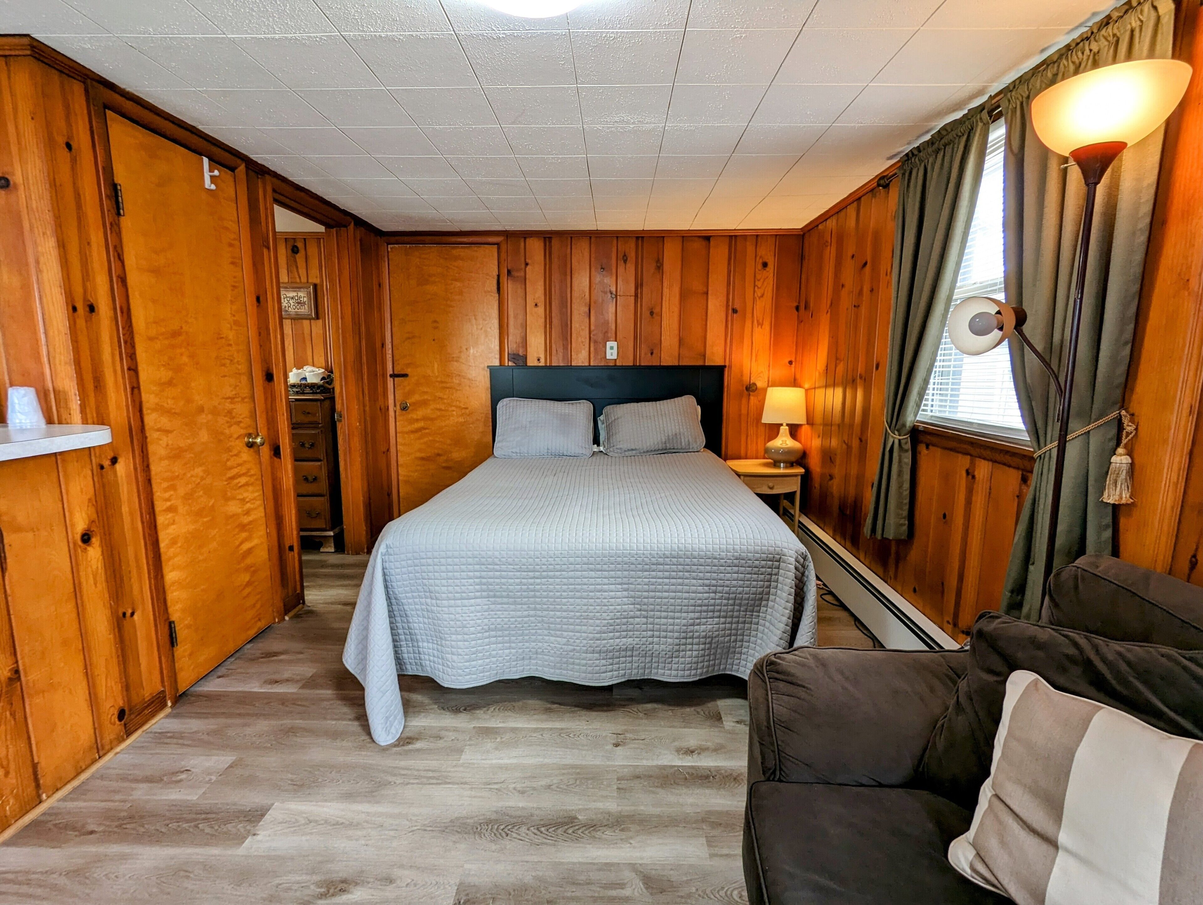 Una stanza con rivestimenti in legno, un letto, un comodino, una lampada e una finestra con tende.