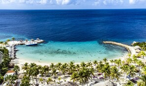 Un complexe hôtelier de bord de mer doté d’un quai pour bateaux, d’une eau turquoise cristalline et de palmiers.