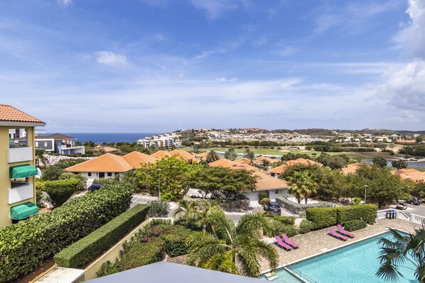 Un resort con piscina, abundante vegetación y vista al mar.
