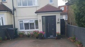 Propiedad residencial con camino de entrada pavimentado, puerta principal y plantas en macetas.