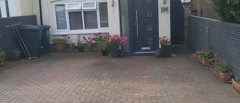 A residential property with a paved driveway, a front door, and potted plants.