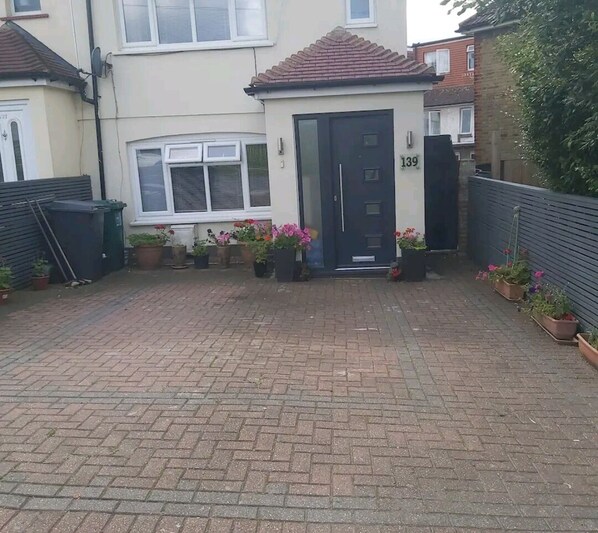 A residential property with a paved driveway, a front door, and potted plants.