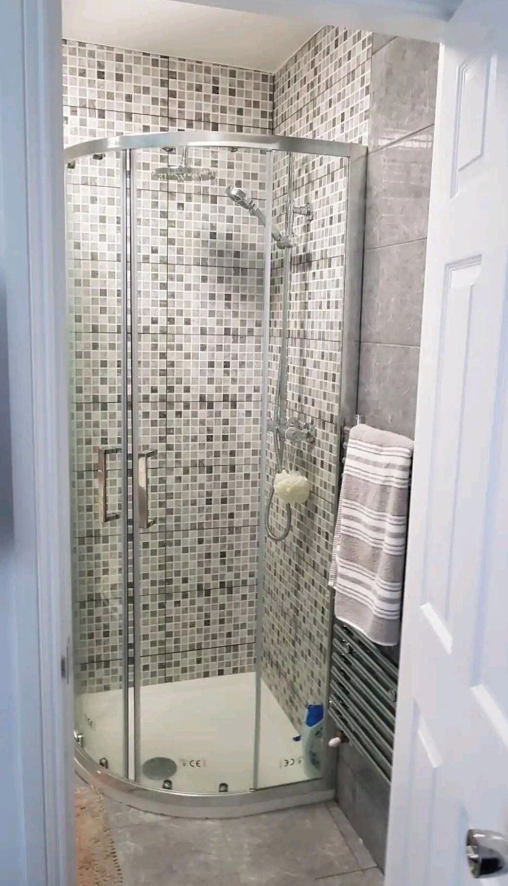 A glass-enclosed shower with a tiled mosaic wall, a towel rack, and a door to the right.