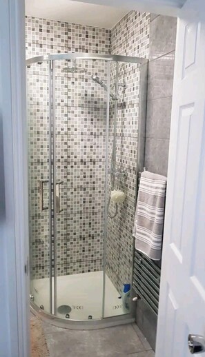 Box de vidro com parede em mosaico de azulejos, porta-toalhas e porta à direita.