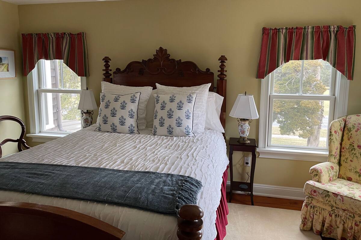 A bedroom with a large bed, two bedside tables with lamps, a chair, and a window with curtains.