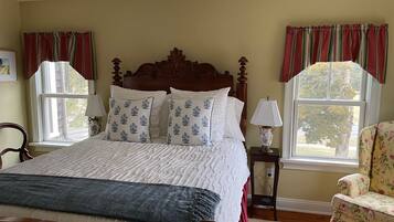 A bedroom with a large bed, two bedside tables with lamps, a chair, and a window with curtains.
