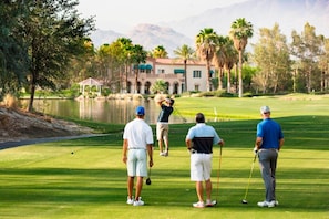 A golf course with a pond, palm trees, and a building in the background.