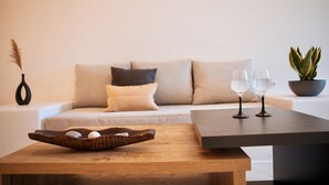 Een moderne woonkamer met een houten salontafel, een bank met kussens, een potplant en twee wijnglazen op een bijzettafeltje.