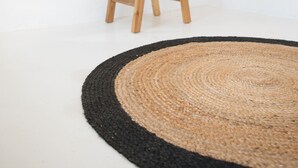 Een kamer met een rond geweven vloerkleed, een houten kruk met tijdschriften en een witte bank.